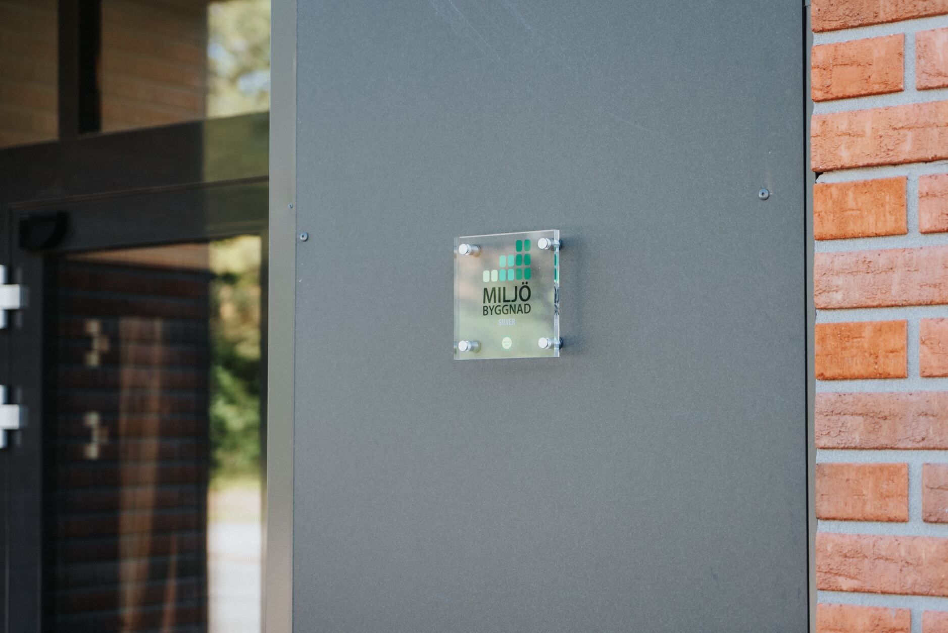 Hållbarhetscertifierad arkitektbyrå. Byggnad av tegel med miljöcertifieringsplakat i glas på framsidan