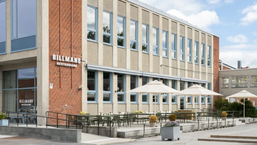 Utsida av restaurangyta med vita parasoll och skylt på framsidan